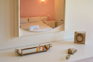 A bedroom with a bed, bedside table, and a mirror reflecting the room.