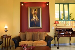 A room with a sofa, a desk, a lamp, and a framed painting on the wall.