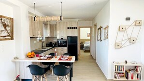 A modern kitchen with a central island, black chairs, and a bookshelf.