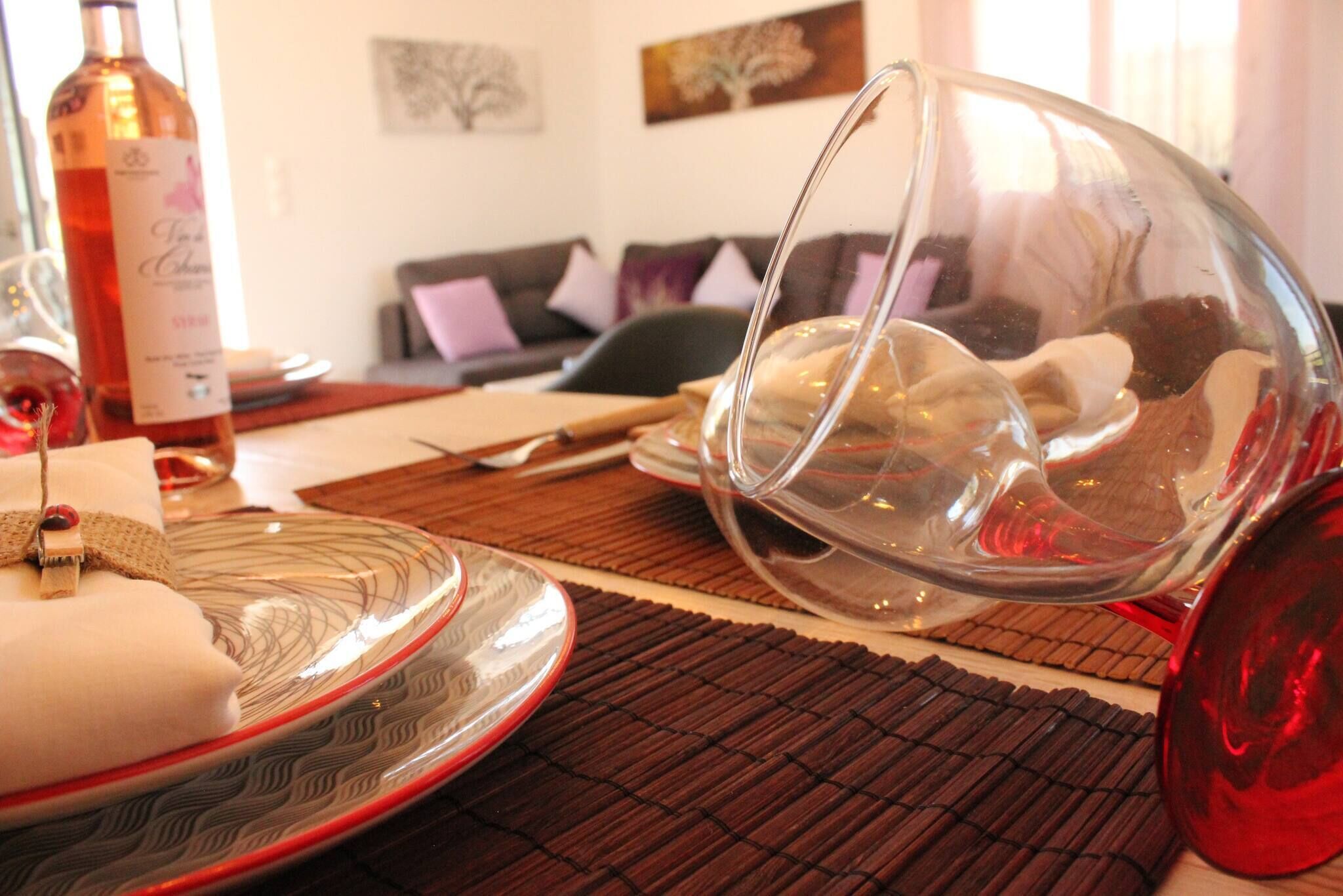 A dining table with a wine bottle, a glass bowl, and a plate with a napkin.