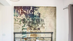 A neatly made bed with a headboard, a bedside table with a lamp, a wall with a vintage map, and a hanging light fixture. - Secret Loft, 2min Walk From The Beach, High Tech (Chania)