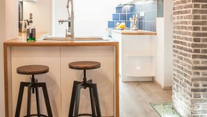 A modern kitchen with a central island, two stools, a brick accent wall, and pendant lighting. - Secret Loft, 2min Walk From The Beach, High Tech (Chania)