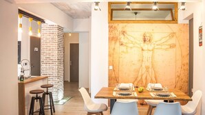 A dining area with a wooden table set for four, white chairs, and a large wall painting of a human figure. - Secret Loft, 2min Walk From The Beach, High Tech (Chania)