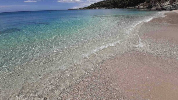 Una playa con aguas transparentes, una orilla arenosa y un paisaje montañoso al fondo.