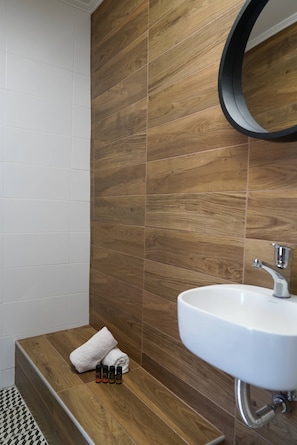 A bathroom with a wooden wall, a white sink, and a towel on a bench. - The Suite Spot - At The Heart Of The Old Town (Chania)