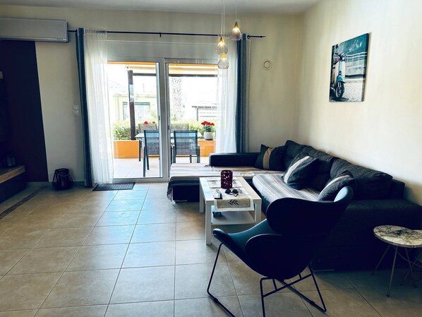A modern living room with a sofa, a coffee table, and a chair. There is a sliding glass door leading to an outdoor area with a table and chairs.