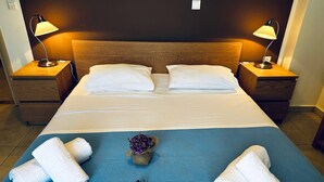 Una habitación de hotel con una cama grande, dos mesitas de noche, dos lámparas y una colcha azul.