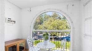 Een balkon met een wit metalen hekwerk, een houten bank en twee witte stoelen met een tafeltje.