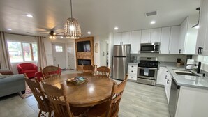 Una cocina moderna con armarios blancos, electrodomésticos de acero inoxidable y un comedor con sillas de madera y una mesa redonda.