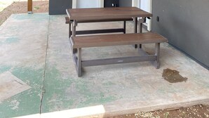 Un patio techado con mesa y bancos de madera, una puerta y una ventana con lámpara.