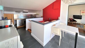 A modern kitchen with a red accent wall, a dining area with a white table, and a TV in the living room.