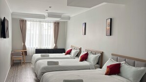 A hotel room with three beds, a round dining table, a TV, and a window with curtains. - AWA Hotel (Rotorua)