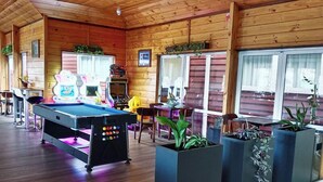 A pool table with a colorful ball return system, surrounded by chairs and potted plants in a wooden room with large windows. - AWA Hotel (Rotorua)