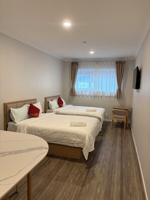 A hotel room with two beds, a small table, a chair, a TV, and a window with curtains. - AWA Hotel (Rotorua)