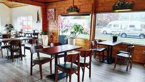 A restaurant with wooden interior, tables, chairs, and potted plants. - AWA Hotel (Rotorua)