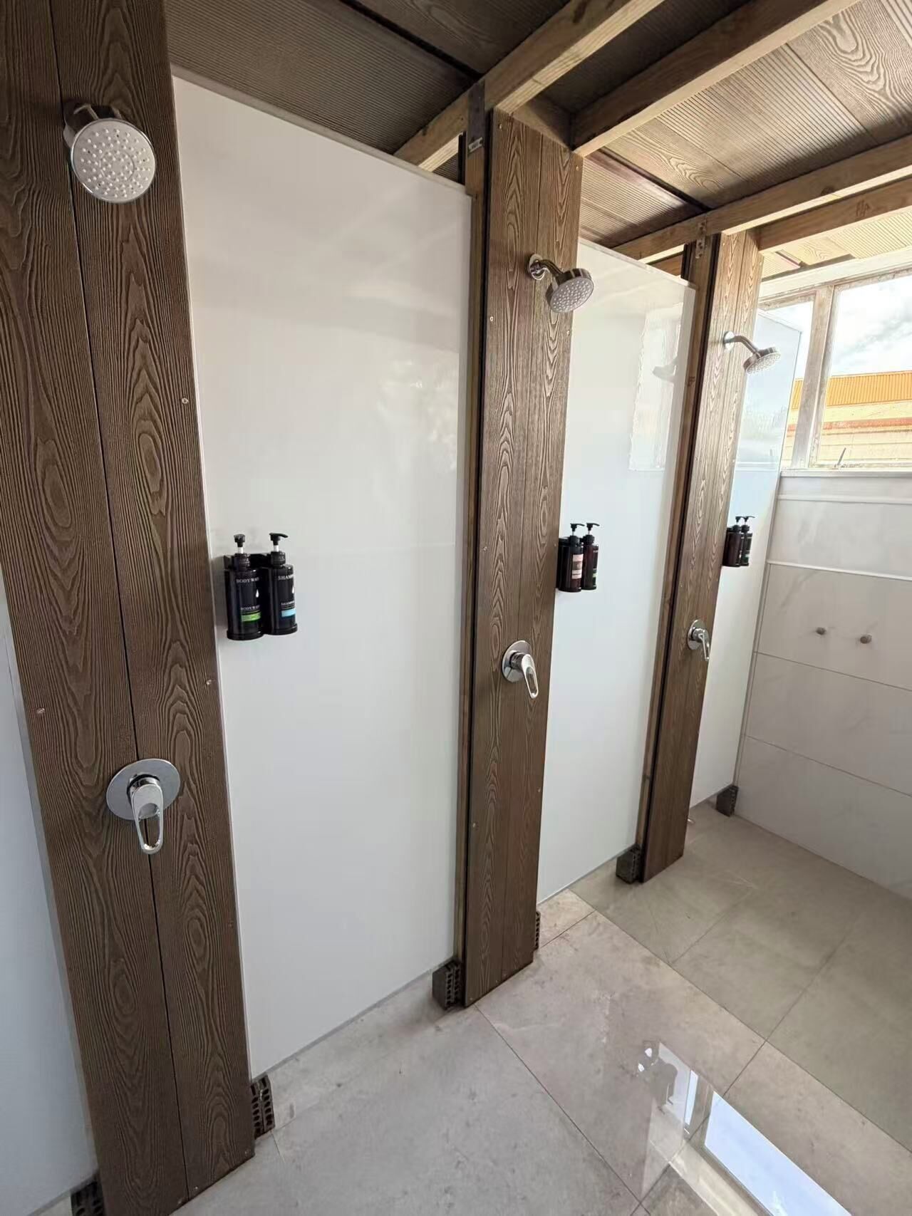 A bathroom with wooden doors, a shower, and toiletries on the wall.