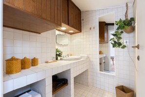 Een badkamer met witte betegelde wanden, houten kastjes, een wastafel, een spiegel en een hangplant.