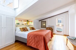 Een slaapkamer met een bed, een radiator, een rieten mand en een tafel met een boek.