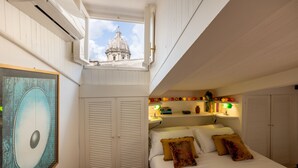 Een slaapkamer met dakraam, een bed met veel kussens, een nachtkastje met een lamp, en uitzicht op een gebouw door het dakraam.