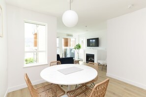 A modern living room with a round white table, wicker chairs, a large white pendant light, and a fireplace. - 2 Bed + DEN 2 Bath Downtown Kelowna (Kelowna)