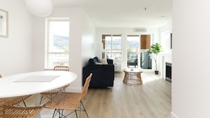 Una sala moderna con una mesa de comedor redonda, sofá azul oscuro, sillas de mimbre y vistas a la ciudad.
