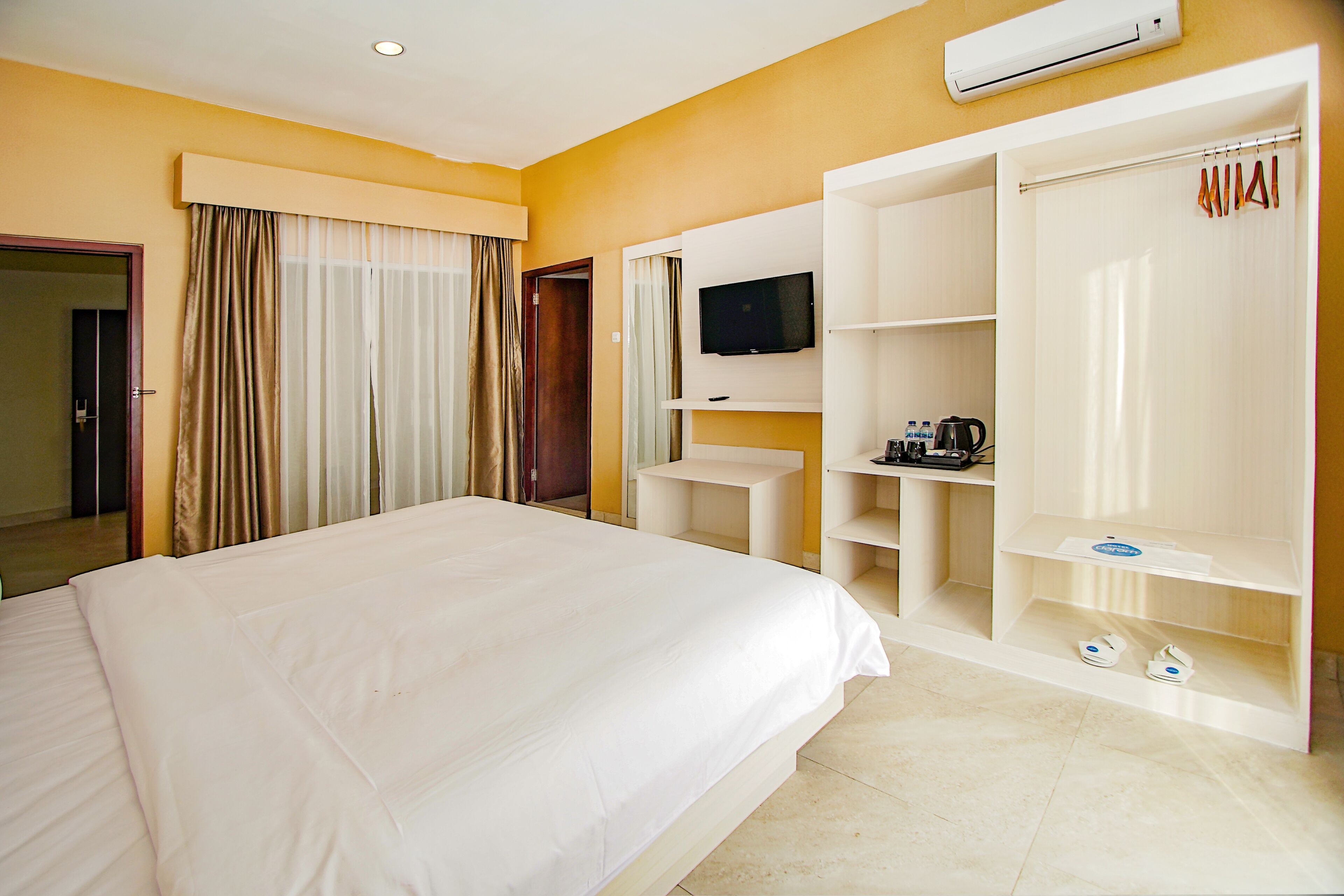 Une chambre d’hôtel avec un grand lit, un téléviseur fixé au mur, une armoire et une étagère contenant des articles de toilette.