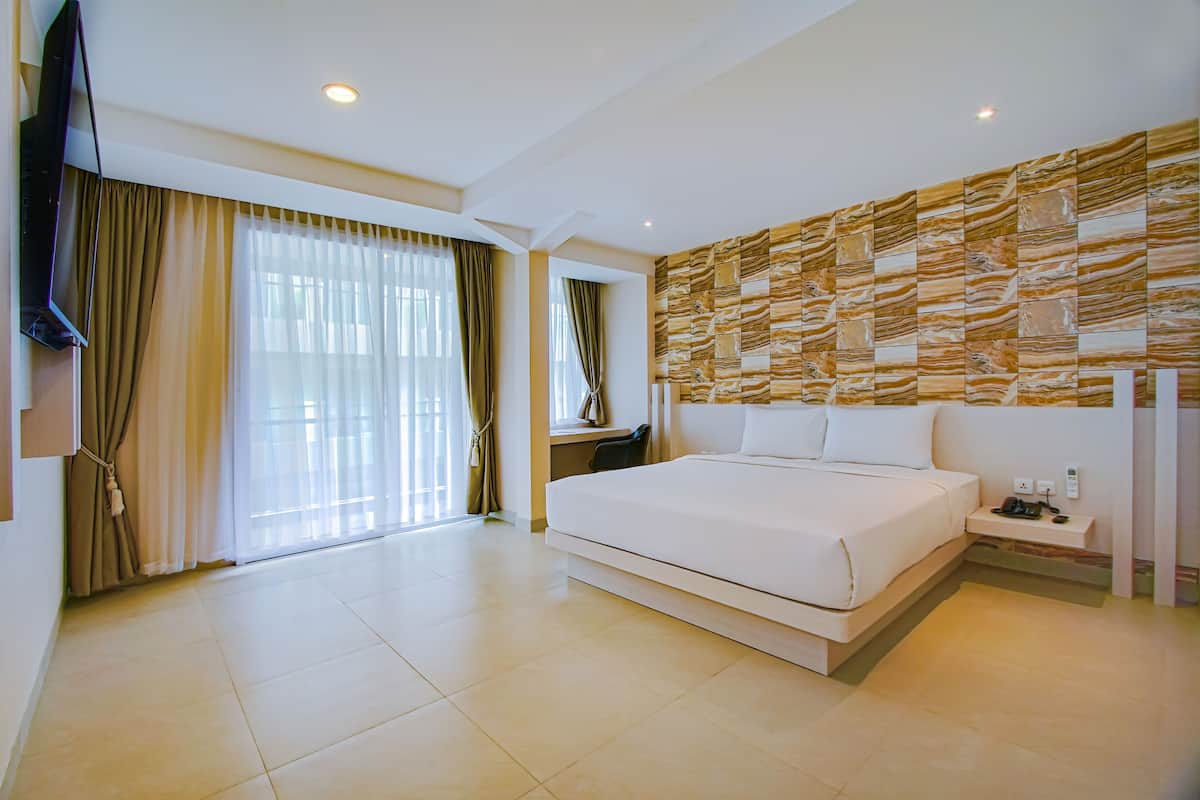 Una habitación de hotel moderna con una cama grande, un televisor de pantalla plana montado en la pared, un escritorio con una silla y un ventanal con cortinas.