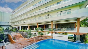 A modern hotel with a large indoor pool, multiple balconies, and lush landscaping.