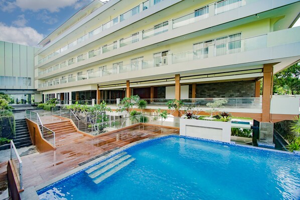 A modern hotel with a large indoor pool, multiple balconies, and lush landscaping.