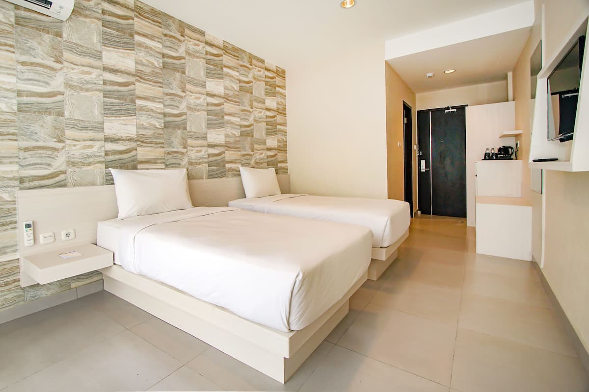 Una habitación de hotel moderna con dos camas, televisión integrada, una mesita de noche pequeña y una pared con diseño de piedra.