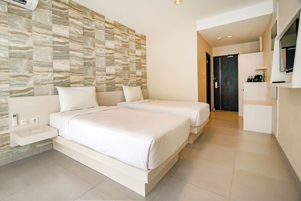 A modern hotel room with two beds, a built-in TV, a small bedside table, and a stone-patterned wall.