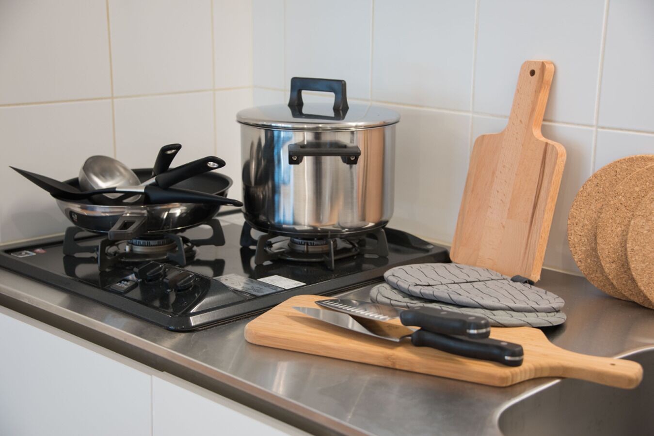 A kitchen with a gas stove, pots, pans, a cutting board, and a wooden spatula.