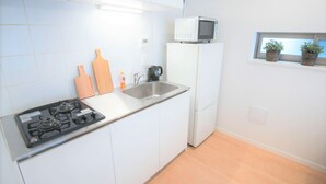 A small kitchen with white cabinets, a gas stove, a microwave, a sink, and wooden cutting boards. - SALON Shibuya 4B (Tokyo)