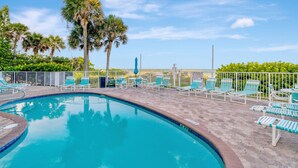 Zona de piscina con sillones de playa y palmeras.