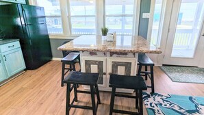 A kitchen with a central island, bar stools, a black refrigerator, and a view through large windows.