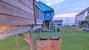 A wooden deck leading to a building with a blue exterior, a fenced area, and a grassy landscape.
