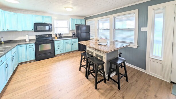 A kitchen with light blue cabinets, a black refrigerator, a microwave, and a granite countertop. There are two black stools at the island.