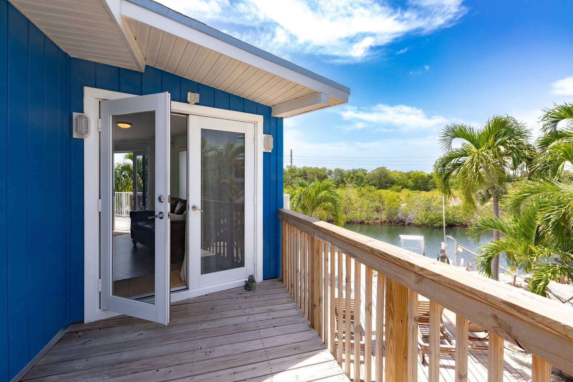 A blue building with a wooden deck overlooking a body of water and greenery.