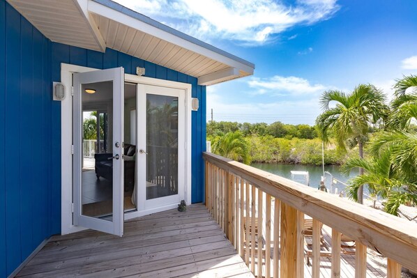 A blue building with a wooden deck overlooking a body of water and greenery.