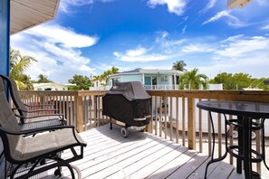 A wooden deck with a grill, chairs, and a table.