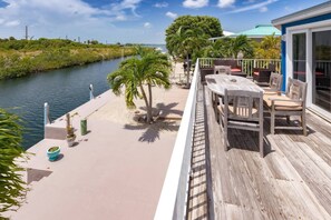 A wooden deck with a table and chairs, overlooking a water body and a distant shoreline.