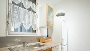 Eine Küche mit Spüle, Holzschränken, einem Fenster mit Spitzenvorhängen, einem Kühlschrank und einem Geschirrständer.