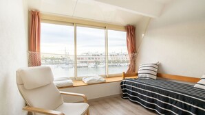 Ein Zimmer mit einem Bett, einem Sessel und einem großen Fenster mit Blick auf einen Hafen.