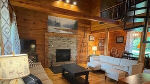 Un intérieur de chalet chaleureux avec une cheminée, un plancher en bois, un canapé et un coin repas.