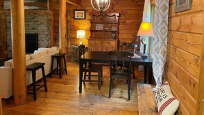 Un intérieur de chalet chaleureux avec un coin repas en bois, une cheminée et une vue sur l’extérieur.