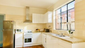 A modern kitchen with white cabinets, a stainless steel refrigerator, a gas stove, and a window with a view of a brick building. - Bay Rd | Kids & Pet Friendly | Free Parking (Cheltenham)