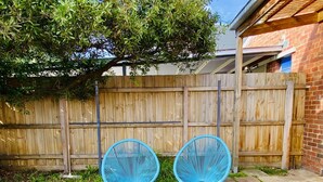 A wooden fence, two blue chairs, and a patio area with stone tiles. - Bay Rd | Kids & Pet Friendly | Free Parking (Cheltenham)