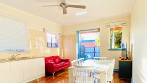A modern kitchen with white cabinets, a red leather sofa, a dining table with white chairs, and a ceiling fan. - Bay Rd | Kids & Pet Friendly | Free Parking (Cheltenham)