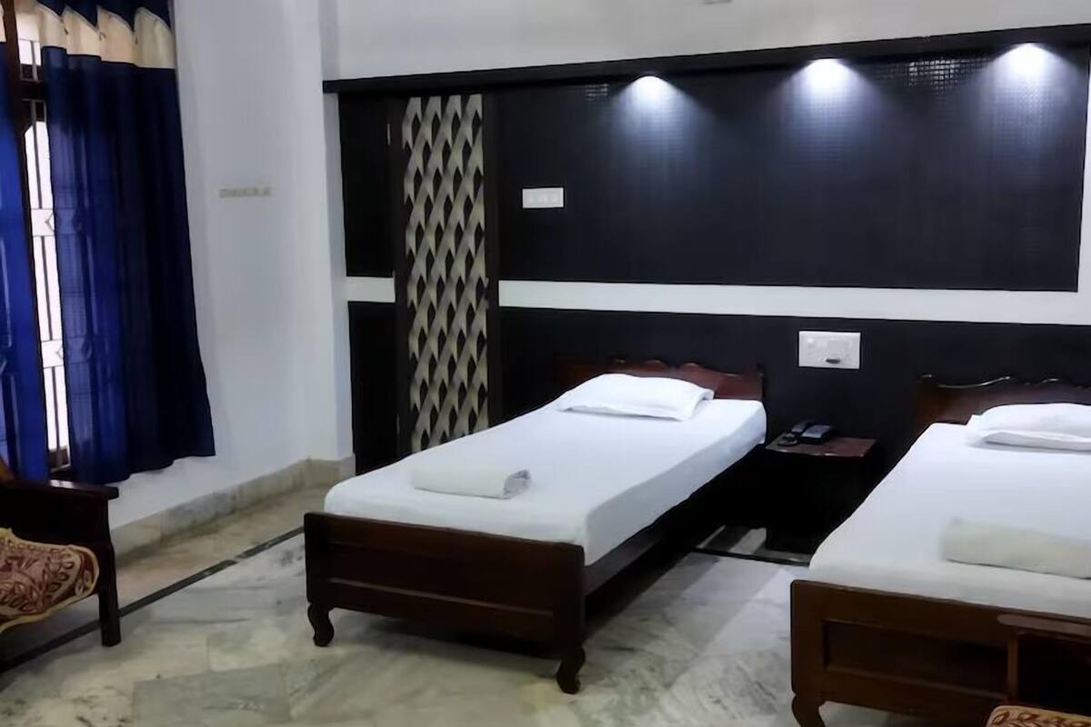 Una habitación de hotel con dos camas individuales, cabecero de madera, cortina estampada y suelo de mármol.