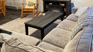A living room with a large flat-screen TV mounted on the wall, a wooden rocking chair, a dark coffee table, and a grey sofa. - Creekside Stay in Walker, MN (Walker)